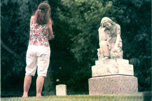 Woman looking at angel grave marker of teenage girl